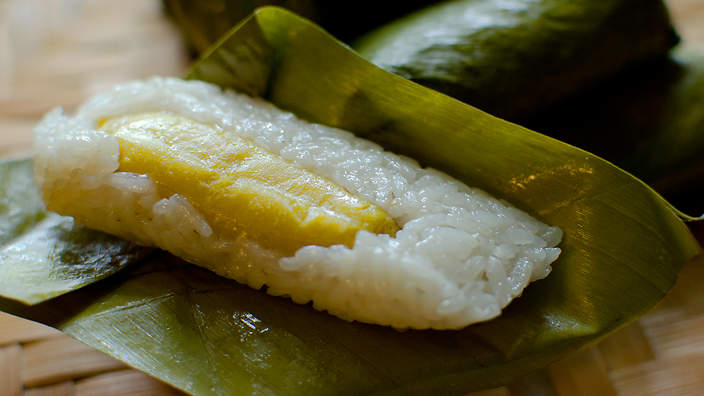 A lump of sticky rice with a piece of banana in it, sitting on a banana leaf